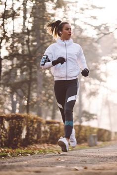 a woman running down a road with trees in the background