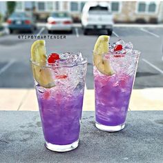 two glasses filled with purple liquid and lemon wedges on top of a cement ledge