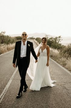 a bride and groom walking down the road holding hands