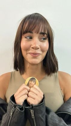 a woman holding a doll in her hand and wearing a leather jacket over her shoulders