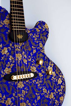 a blue and gold guitar sitting on top of a white wall