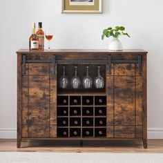 a wooden cabinet with wine glasses and bottles on it in front of a white wall