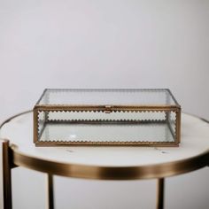 a glass and brass box sitting on top of a white table with a gold frame