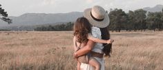 two women are standing in a field with mountains in the background and one has her back to the camera