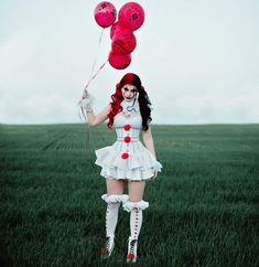 a woman with red hair and makeup is holding two pink balloons in the middle of a field