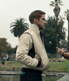 two men standing next to each other in front of a pond and some palm trees