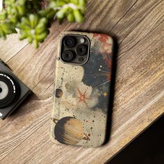 an iphone case sitting on top of a wooden table next to a camera and plant