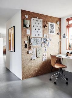 a room with a desk and chair next to a corkboard wall that has pictures on it