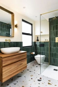 a bathroom with green tile and wooden cabinetry, sink, toilet and shower stall