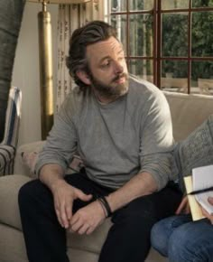 a man sitting on top of a couch next to another man holding a clipboard