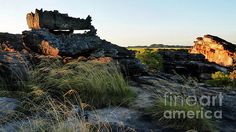 the sun is setting on some rocks and grass in the foreground, with an outcropping to the right