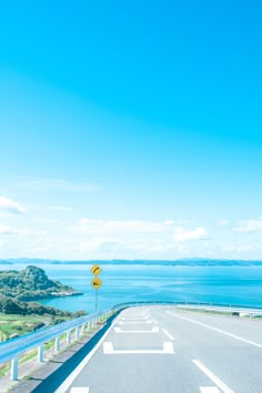 an empty road near the ocean on a sunny day with blue sky and water in the background