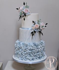 a three tiered white and blue cake with flowers on top