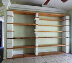 a room with some shelves and a ceiling fan in it's corner, next to a tile floor