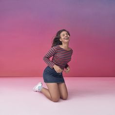 a woman is laughing while sitting on the floor in front of a pink and blue background