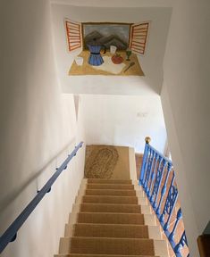 a staircase with blue railings leading up to a painting on the wall above it