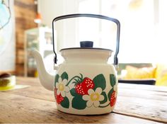 a tea pot with flowers painted on it sitting on a wooden table in front of a window