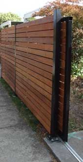 a wooden fence is shown in front of some bushes and trees on the side walk