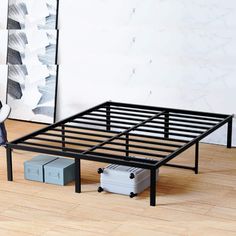 a black metal bed frame sitting on top of a hard wood floor next to a painting