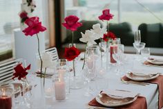 the table is set with red and white flowers in vases, candles, and plates