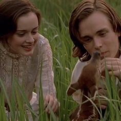 a young man and woman sitting in tall grass with a baby deer on their lap