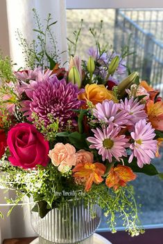 a vase filled with lots of colorful flowers on top of a table next to a window