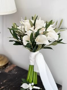 a bouquet of white flowers sitting on top of a wooden table next to a lamp