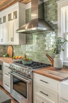 a kitchen with white cabinets and green tile backsplash, stainless steel range hood