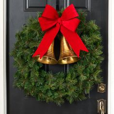 a christmas wreath with two bells hanging from it's side and a red bow on the front door