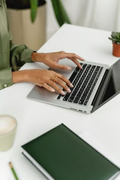 a woman sitting at a table using a laptop computer with her hand on the keyboard