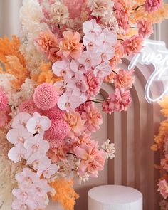 pink and orange flowers are hanging from the ceiling next to a white cake on a table