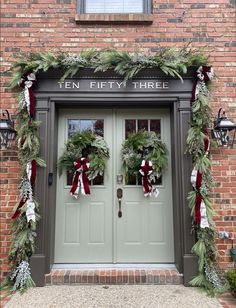 two wreaths are hanging on the front door of a brick building with green doors