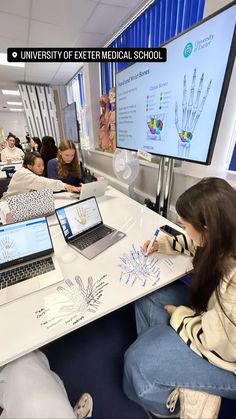 several people sitting at a table with laptops in front of them and on the screen