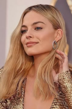 a woman with long blonde hair wearing large hoop earrings and gold sequind dress