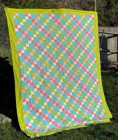 a green and pink quilt sitting on top of a lush green field