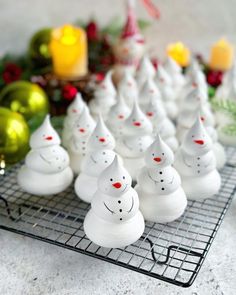 small white ceramic snowmen sitting on a wire rack next to christmas decorations and candles