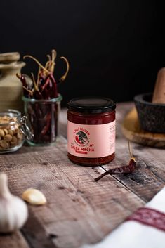 a jar of jam sitting on top of a wooden table next to garlic and pepper