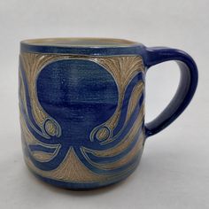 a blue and gold coffee mug with an octopus on it's side sitting on a white surface