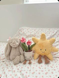 two stuffed animals sitting on top of a bed next to a potted plant and flower