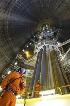 a man in an orange jumpsuit standing next to a tall metal structure