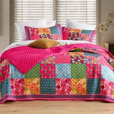 a bed covered in pink and green patchwork quilts next to a window with white blinds