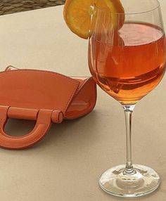 an orange slice sitting on top of a wine glass next to a leather case and bottle opener