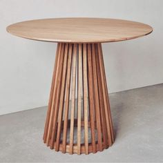 a round wooden table sitting on top of a cement floor next to a white wall