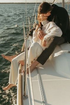 a man and woman sitting on the back of a sailboat kissing each other in front of water