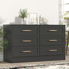 a large black dresser with gold handles in a living room next to a potted plant