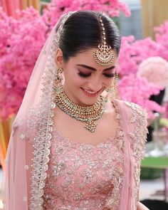 a woman wearing a bridal outfit with jewelry on her neck and headpiece, in front of pink flowers