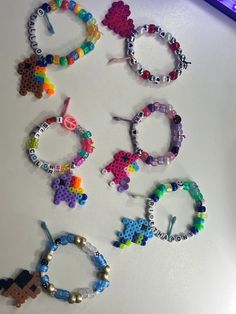 six pairs of beaded bracelets are arranged on a white surface next to a pencil