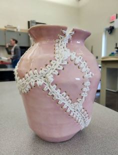 a pink vase sitting on top of a counter in a room with people working behind it