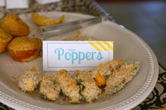 a plate topped with muffins next to a paper sign that says poppers