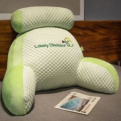 a large green teddy bear sitting on top of a bed next to a book and magazine